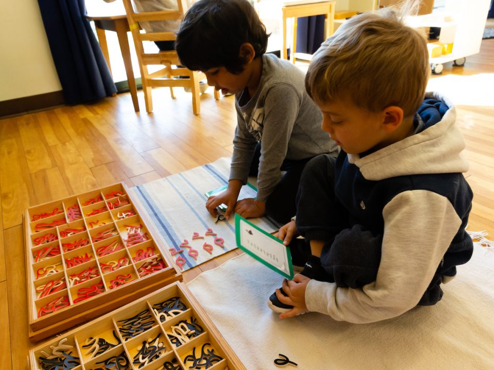 two boys writing using wooden cursive letters in a Montessori Classroom