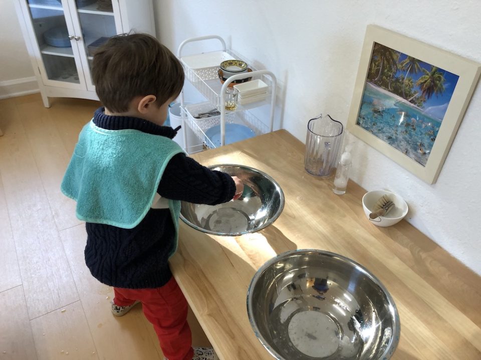 Toddler learning to conserve water by using two bowls to clean