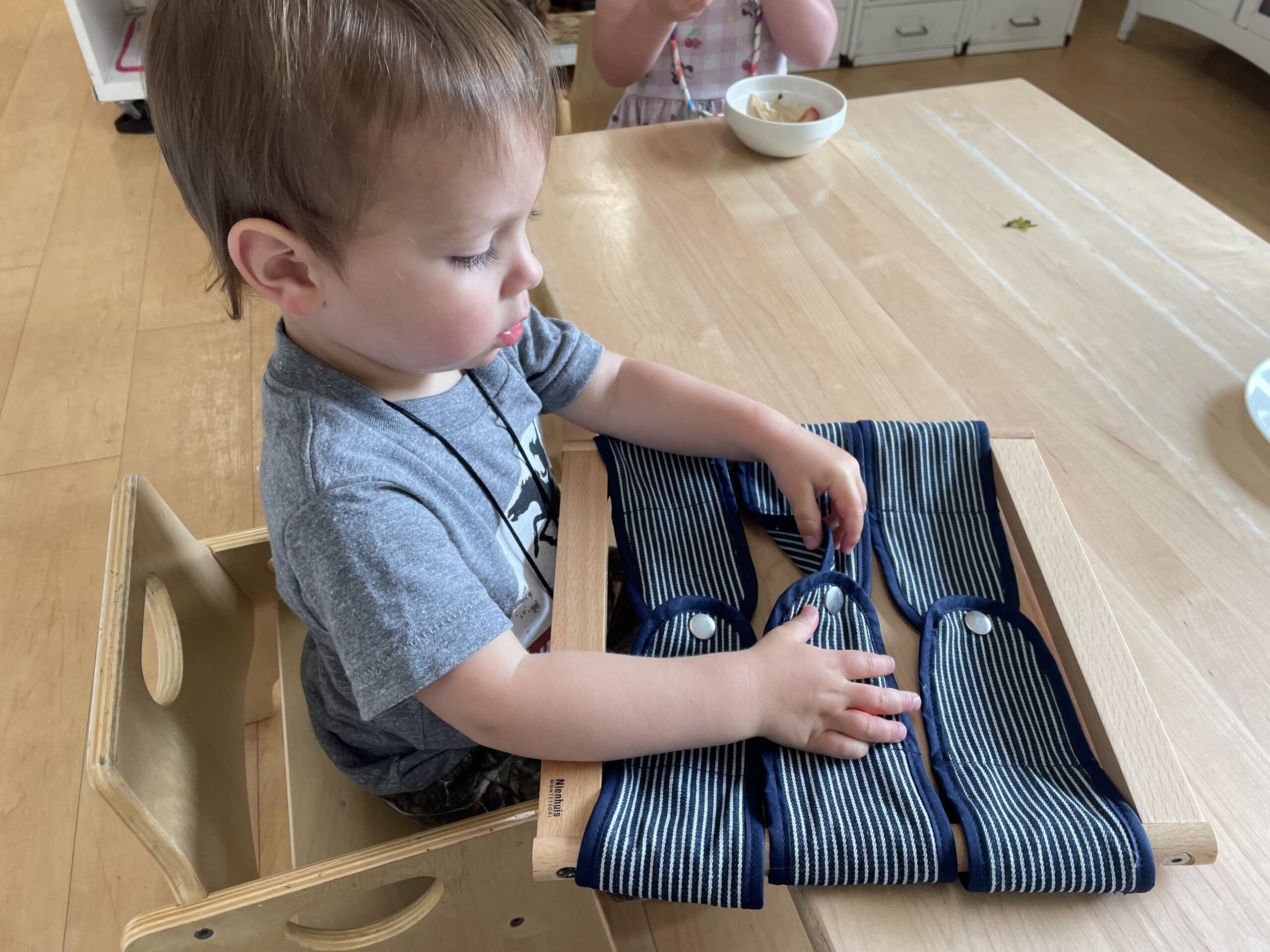 Best Age To Start Preschool. Toddler learning how to snap buttons.