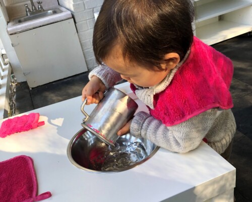 Toddler independently pouring water into sink