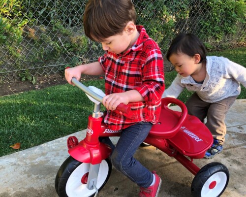 Toddlers riding a trike in a Montessori playground
