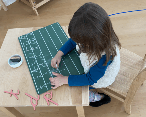 Niño pequeño en preescolar Montessori aprendiendo la letra cursiva