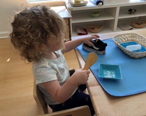 Toddler learning how to clean her shoes at preschool
