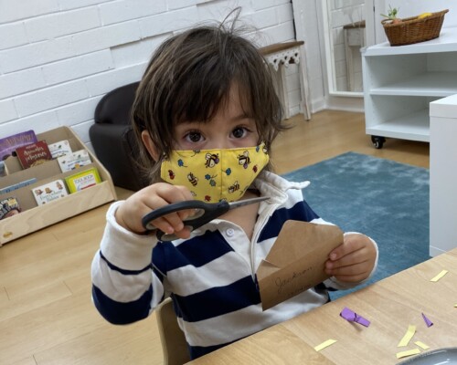 Toddler boy using scissors independently in a Montessori preschool